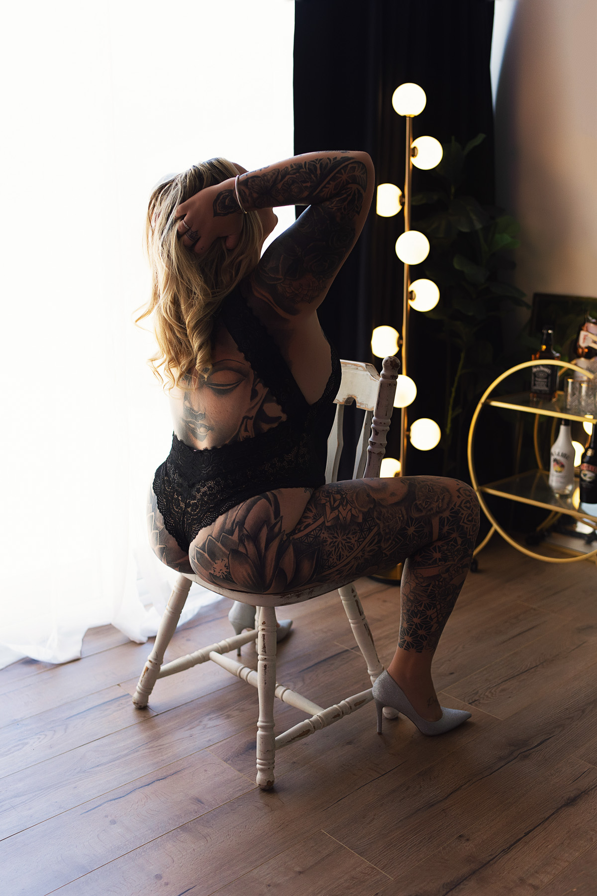 Boudoir client with tattoos on chair, back arched. Luxury photography experience in Upper Coomera.