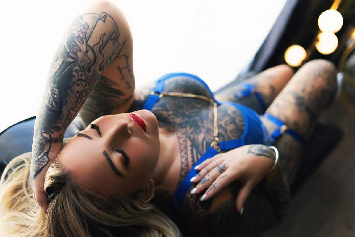 Boudoir client with tattoos reclining on lounge, calm and confident. Photo session on the Gold Coast.