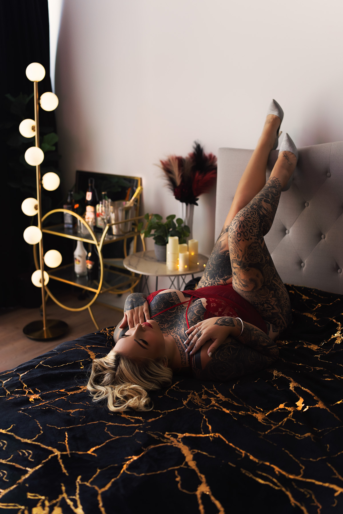 Boudoir client with tattoos in red lingerie, lying on bed. Glamour photography on the Gold Coast.
