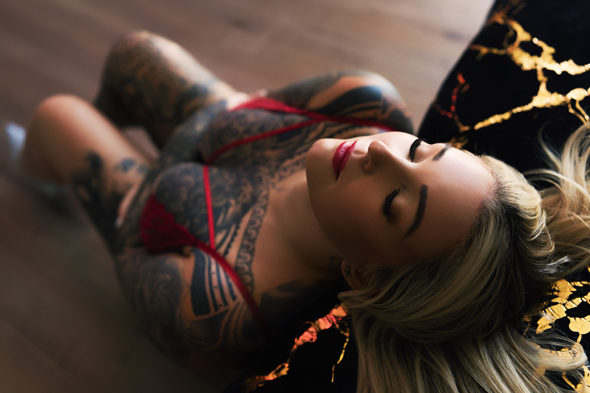 Boudoir client with tattoos in red lingerie, sitting on floor. Glamour photo session in Gold Coast studio.