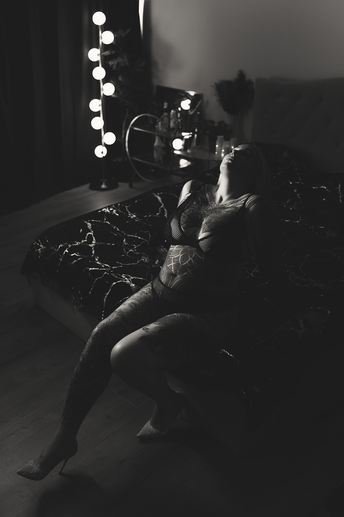 Woman sitting on bed with dark contrasty lighting in black and white photo. Boudoir photography on the Gold Coast.