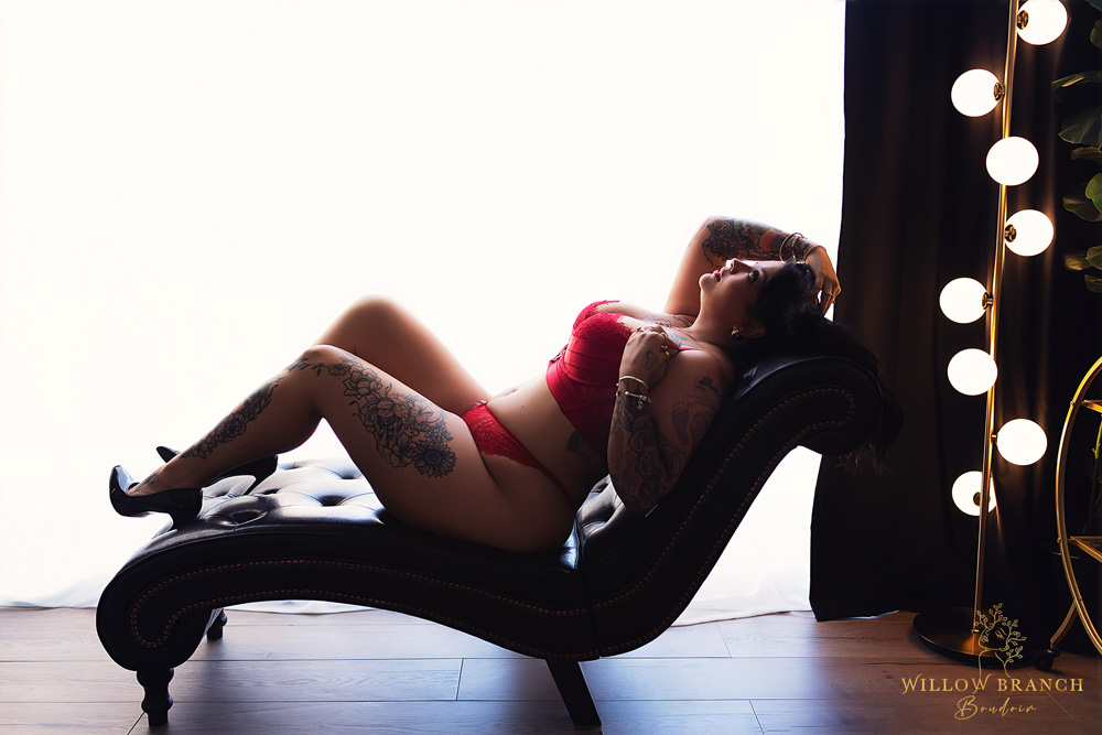 Woman treating herself to a self care boudoir shoot to reconnect with herself, reclining on lounge in red lingerie.