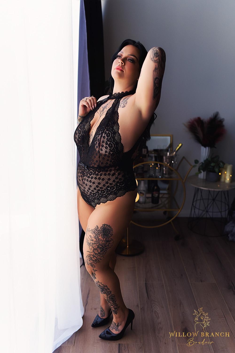 Gold Coast boudoir photography of woman in black lingerie outfit in studio, standing by window with natural light