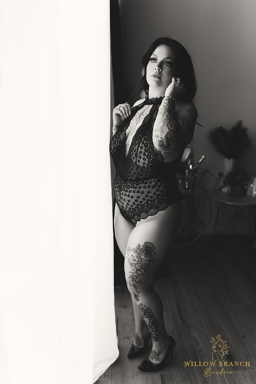 Gold Coast boudoir photo of woman in black lingerie in studio, standing by window with natural light, c=black and white photo